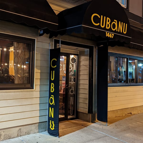 Exterior of CubaNu Restaurant & Lounge at night, with a black awning and yellow lettering.