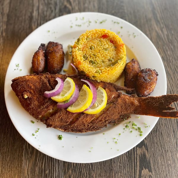 Whole fried fish with lemon and red onion, yellow rice, and fried plantains on a white plate.