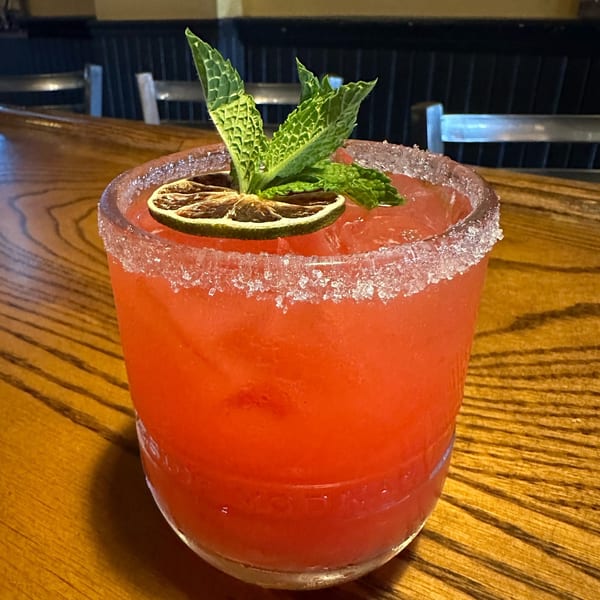 Vibrant red cocktail with a sugar-rimmed glass, garnished with mint and a dried lime slice.