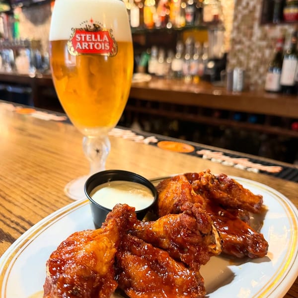 A Stella Artois beer and a plate of glazed chicken wings with dipping sauce on a bar.