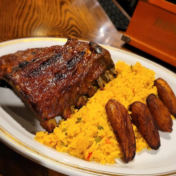 Cuban-style ribs with yellow rice and fried plantains on a white plate.