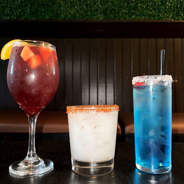 Three vibrant Cuban cocktails: red sangria, white drink with chili rim, and blue drink with sugar rim.