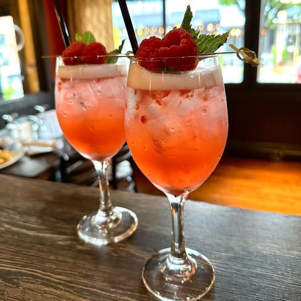Two vibrant red cocktails with raspberry and mint garnishes on a wooden bar at CubaNu Restaurant.
