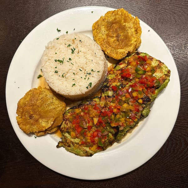 Grilled chicken with colorful salsa, white rice, and two fried plantains on a white plate.