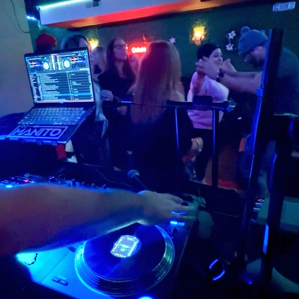 A DJ plays music for a dancing crowd at CubaNu Restaurant & Lounge, illuminated by blue and red lights.