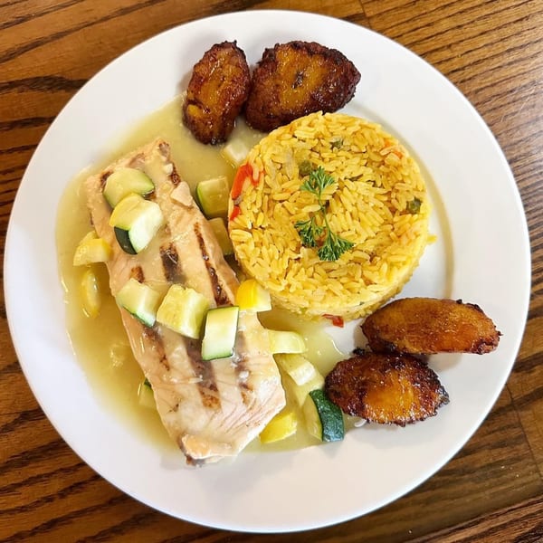 Grilled fish with zucchini, yellow rice, and fried plantains on a white plate at CubaNu Restaurant.