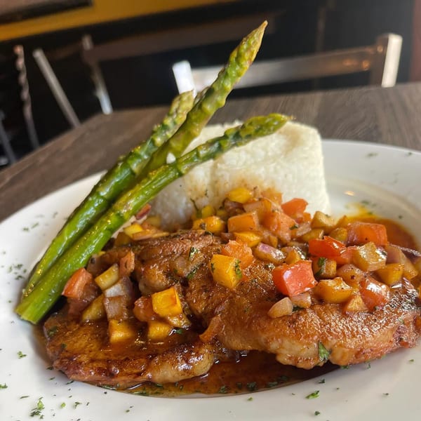 Cuban dish with seared meat, mango salsa, white rice, and asparagus on a white plate.
